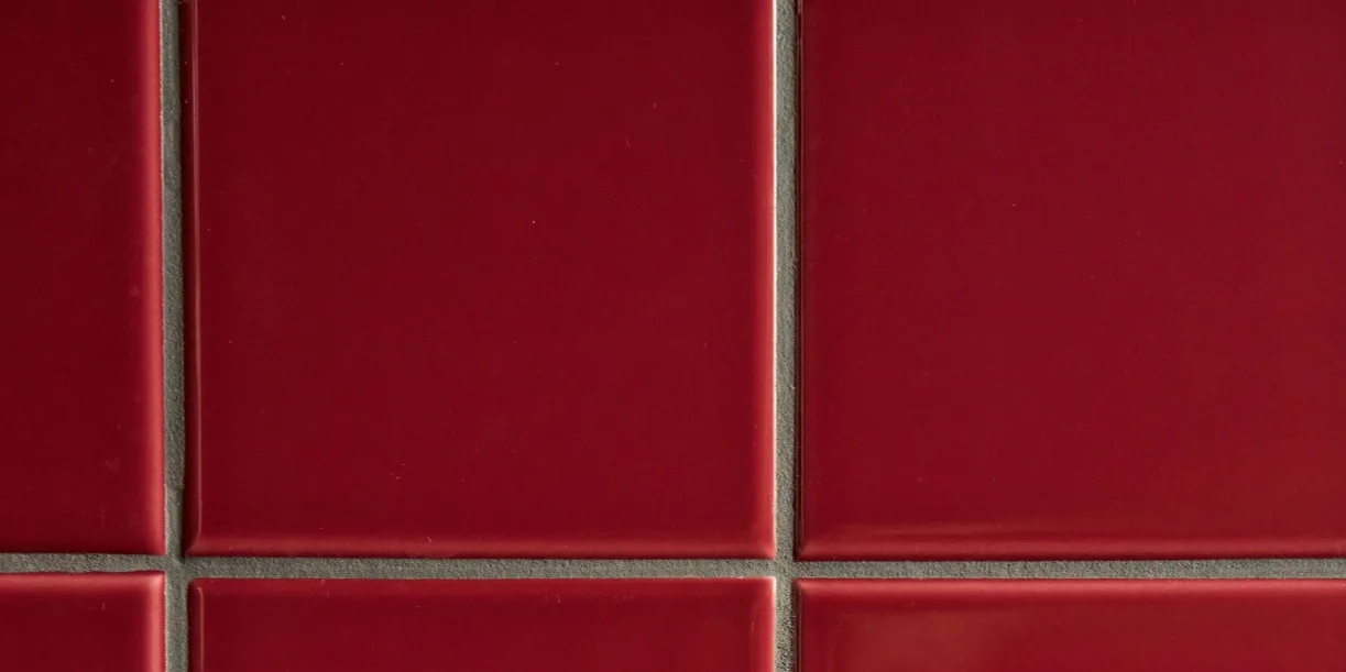 Piastrelle quadrate lucide rosso intenso con fughe grigio chiaro in una griglia.