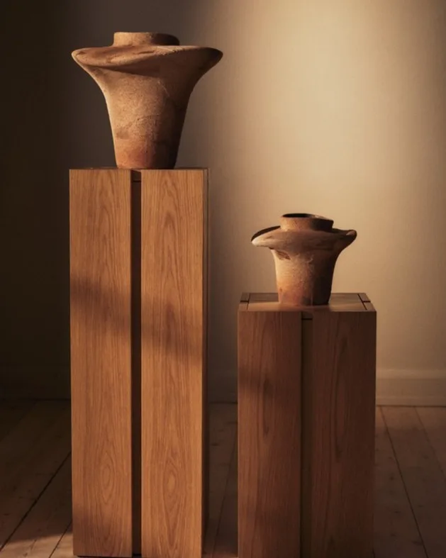 Due vasi in ceramica terrosi e svasati su piedistalli di legno chiaro.