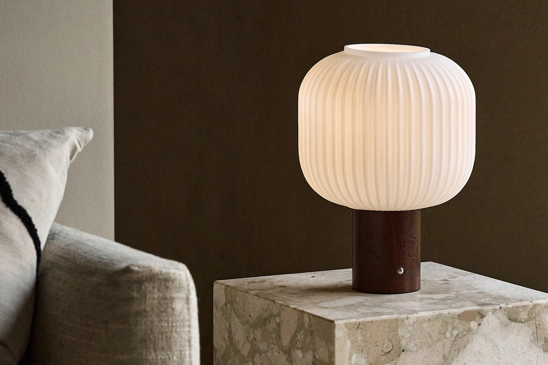 Lampada da tavolo bianca a coste con base in legno su un tavolino in marmo accanto a un divano.