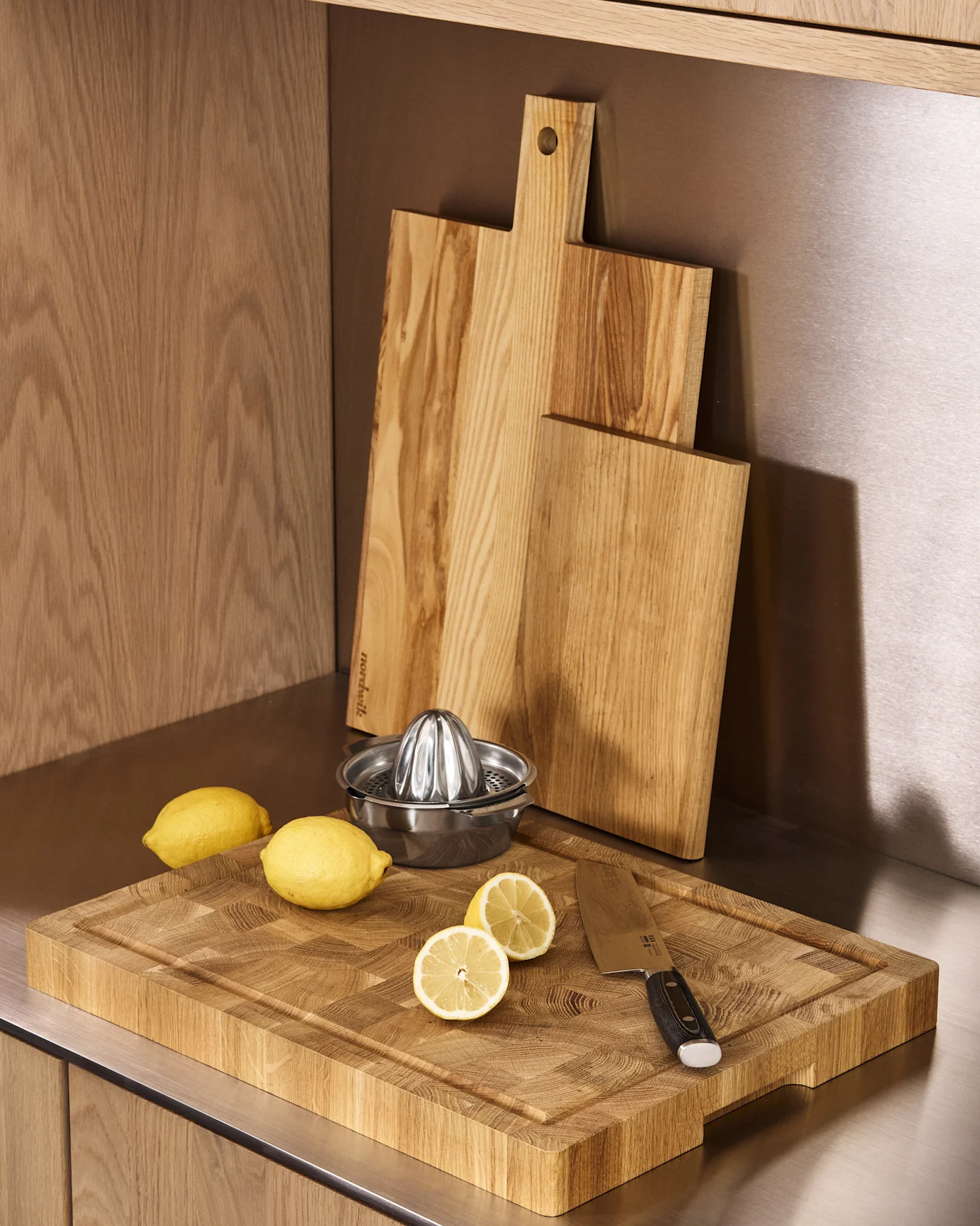 Bancone da cucina con tre taglieri in legno, uno spremiagrumi in metallo, limoni interi e a metà, e un coltello.