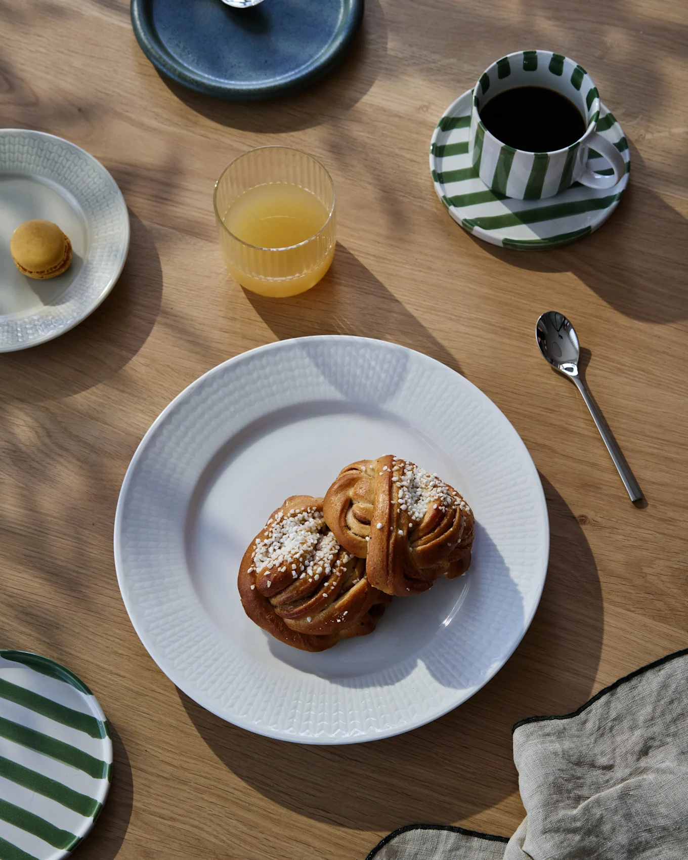 Una colazione su un tavolo di legno con due rotoli alla cannella, caffè in una tazza a strisce, succo d'arancia e un macaron.